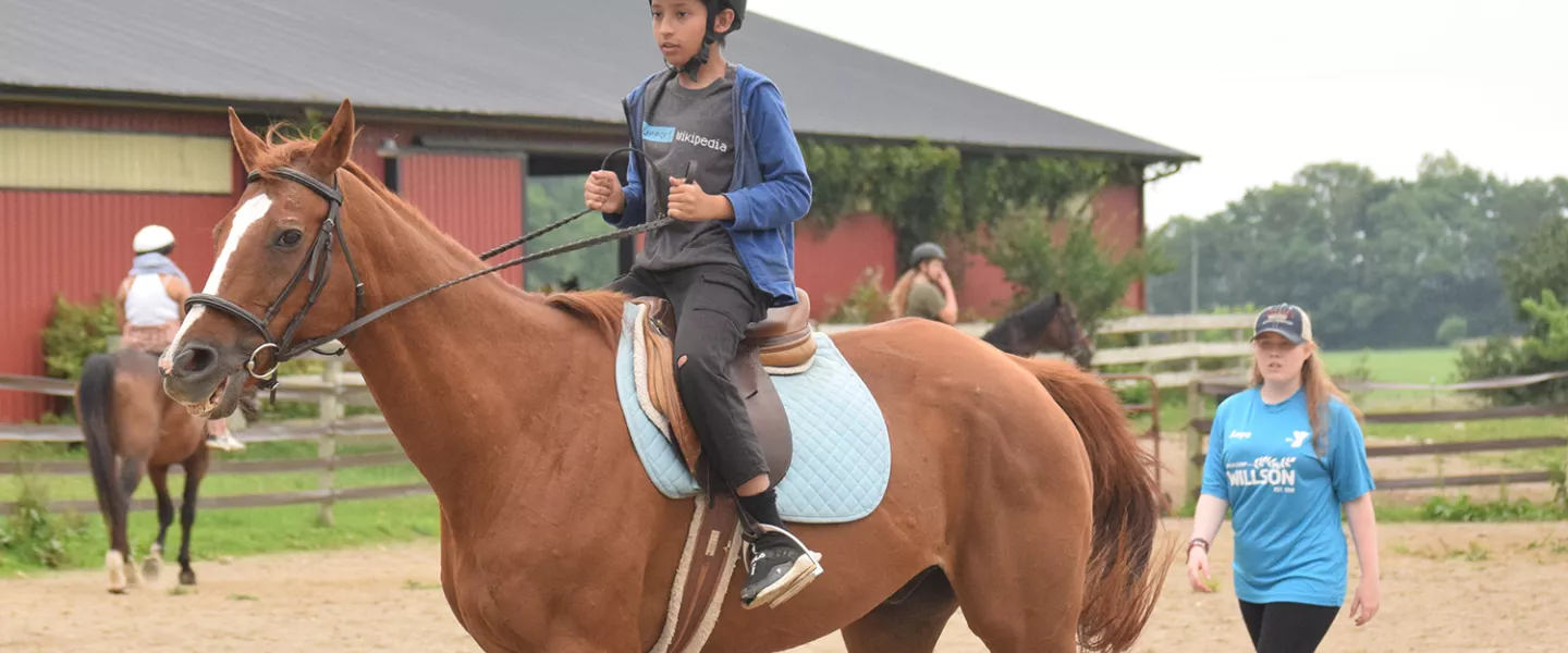 Camper riding a horse while staff watches